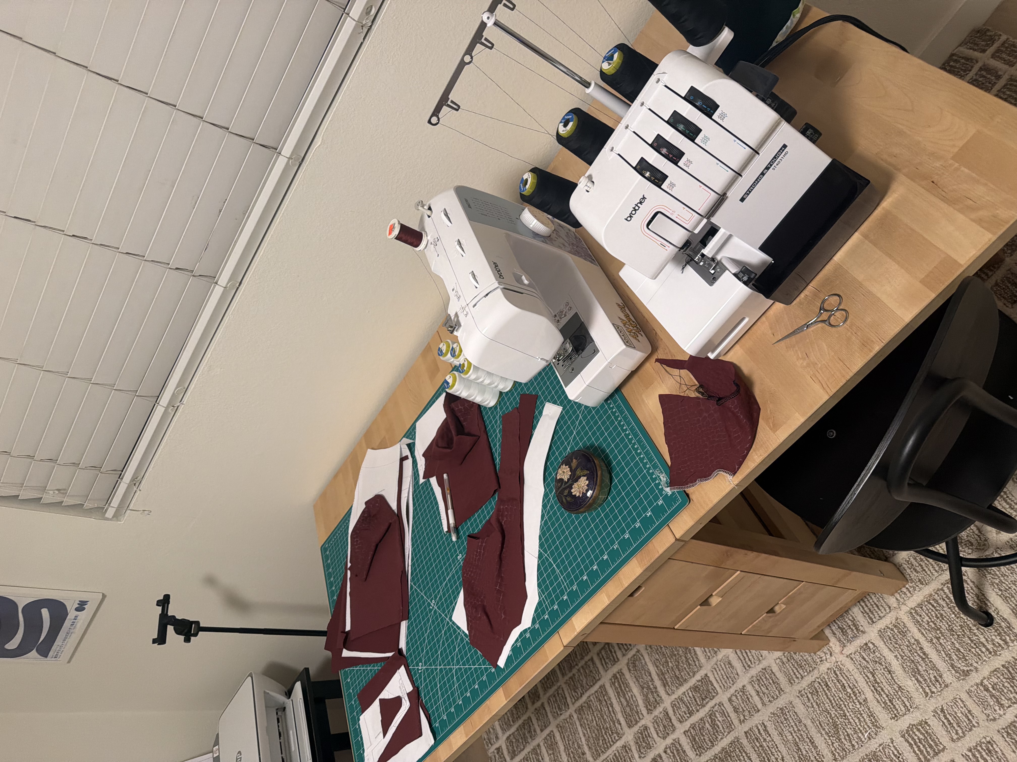 The Becky set pattern pieces cut from the maroon snake print fabric on Emily's cutting table, next to her sewing machine and serger